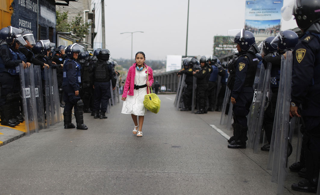 A girl walks past riot policemen guarding one of the access roads to Benito Juarez International airport after demonstrators staged a protest over the 43 missing Ayotzinapa students in Mexico City November 20, 2014. Forty-three missing students abducted by corrupt police in southwest Mexico weeks ago were apparently incinerated by drug gang henchmen and their remains tipped in a garbage dump and a river, the Mexican government said.  REUTERS/Tomas Bravo (MEXICO - Tags: SOCIETY CIVIL UNREST POLITICS TPX IMAGES OF THE DAY)