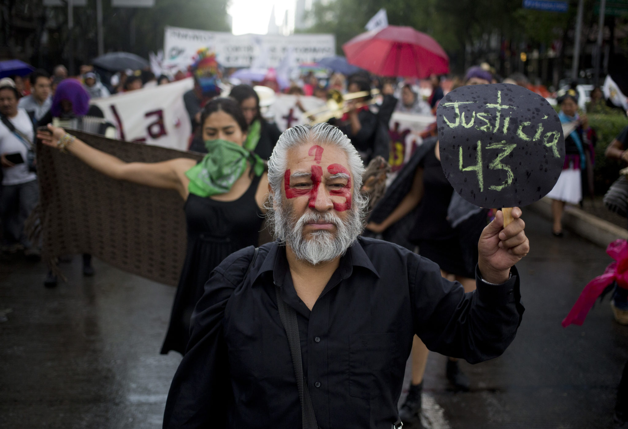 A demonstrator with the number 43 painted on his face and a sign with the word "Justice" written in Spanish in reference to the 43 missing students from a rural teachers college, marches in protest, marking 30 months since their disappearance, in Mexico City, Sunday, March 26, 2017. The federal prosecutor claimed that the students were detained by local police and handed over to a drug gang, who killed them and burned their bodies, but a group of experts from the Inter-American Commission on Human Rights does not agree with that hypothesis. (AP Photo/Eduardo Verdugo)